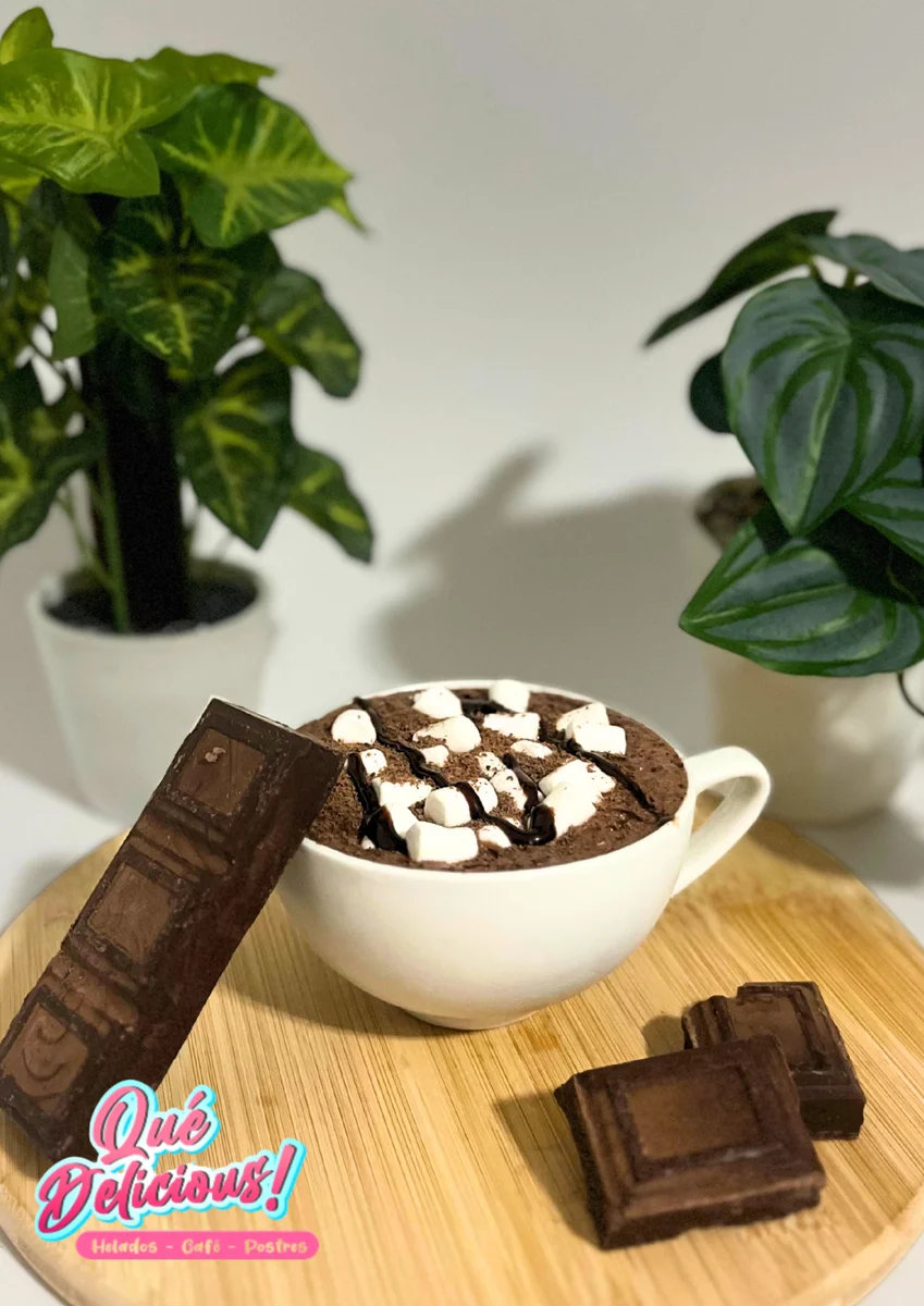 Taza de chocolate caliente premium y café especialidad servidos con crema batida en Que Delicious